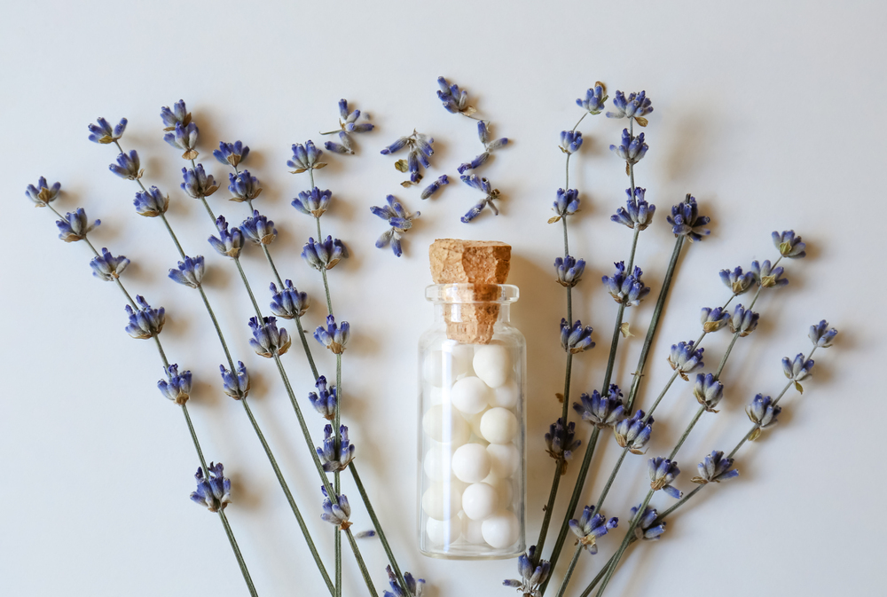 Bottle of homeopathic remedy and lavender on white background, f